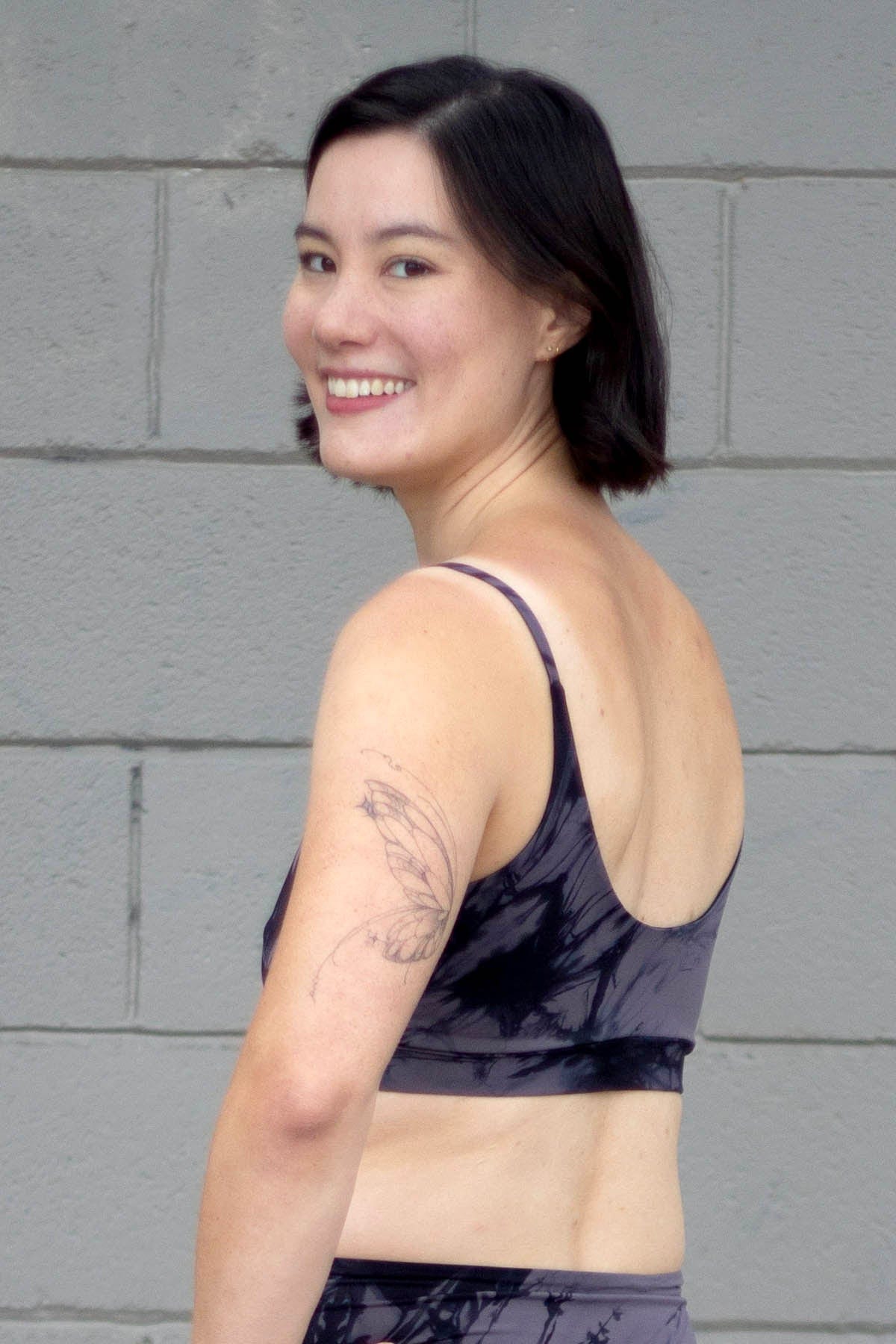 The back of a woman smiling and wearing a grey tie-dye swim top