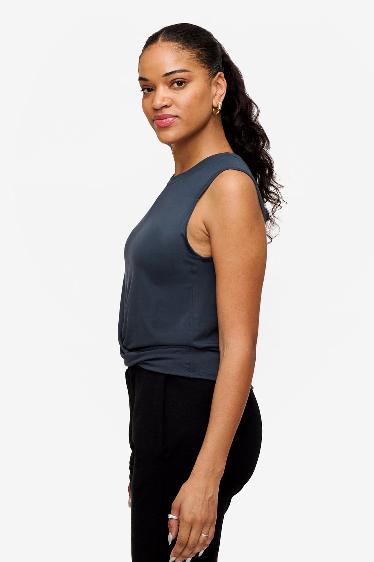 side of a woman wearing a sleeveless shirt with a twist at the front in dark blue