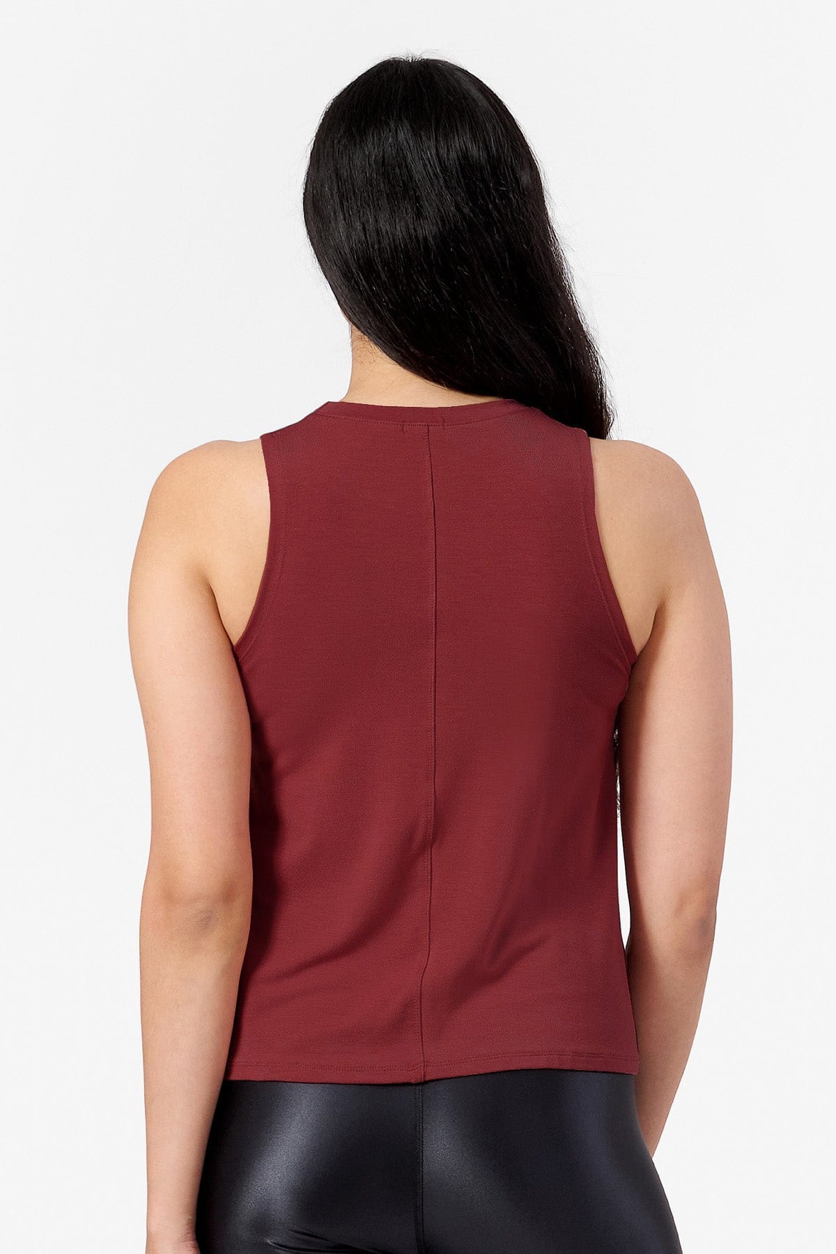 This is a back view of a woman wearing a sleeveless tank top. It is dark red and sits at hip length. It is designed for workout and every day wear.