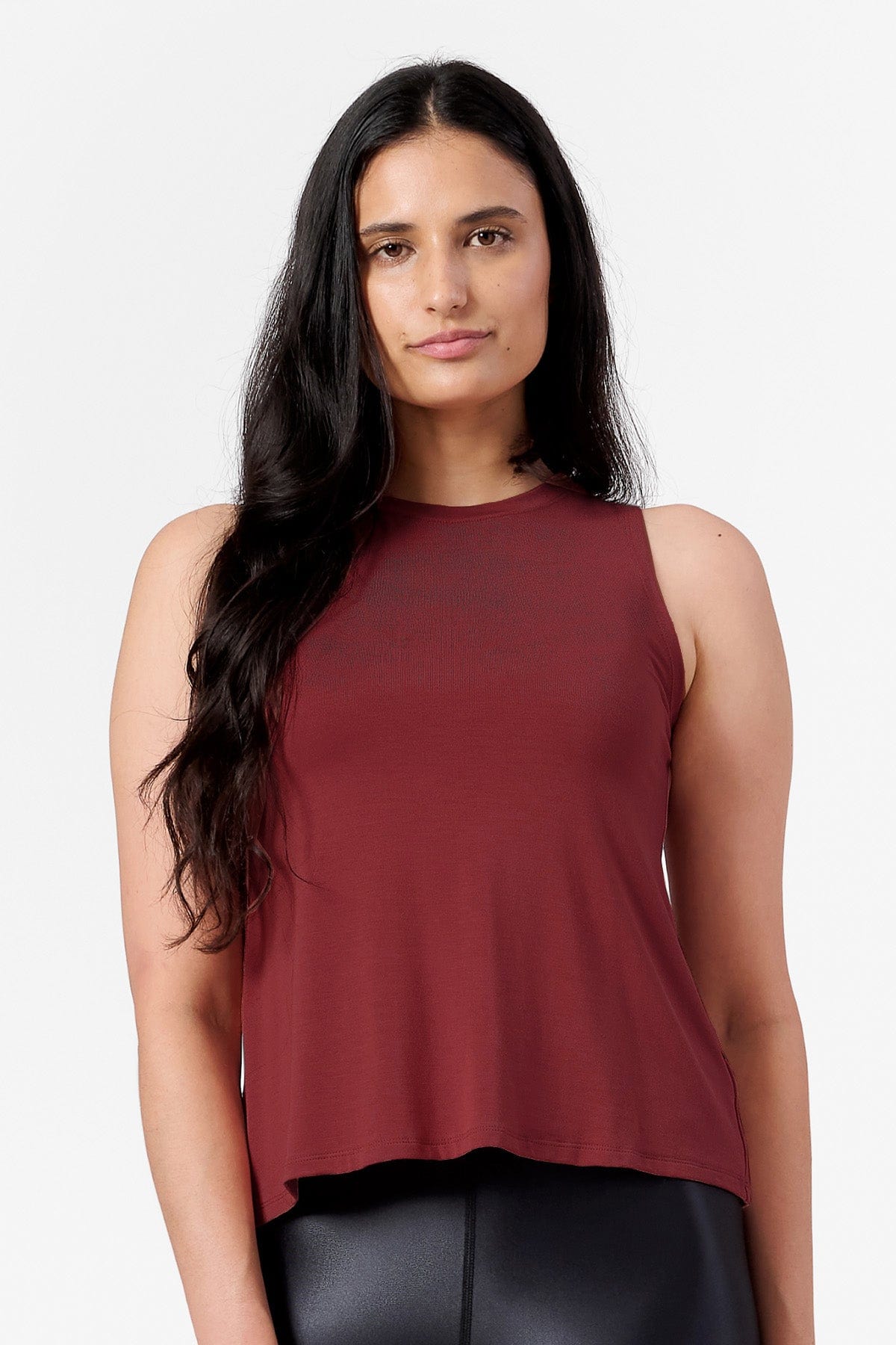 A woman wears a dark red sleeveless tank top that sits loose at the waistline and gently fitted at the bust. It's made in Canada for workouts and everyday clothing.