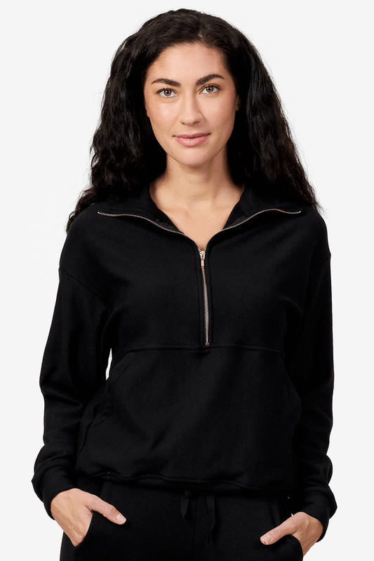 Woman wearing a black half zip sweatshirt with her hands on the pockets