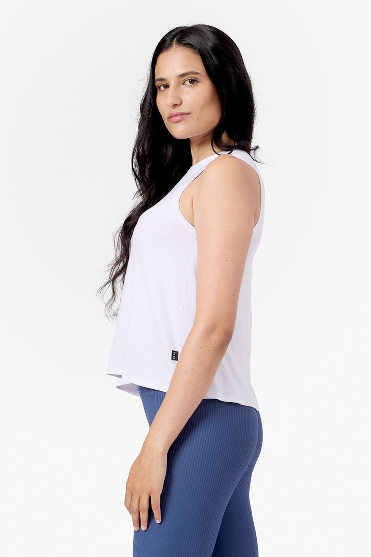 Side of a woman wearing a white tank and blue ribbed leggings