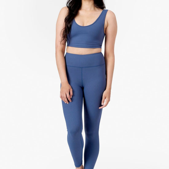 a woman wearing a blue low scoop crop top with lining and a matching blue ribbed pair of leggings