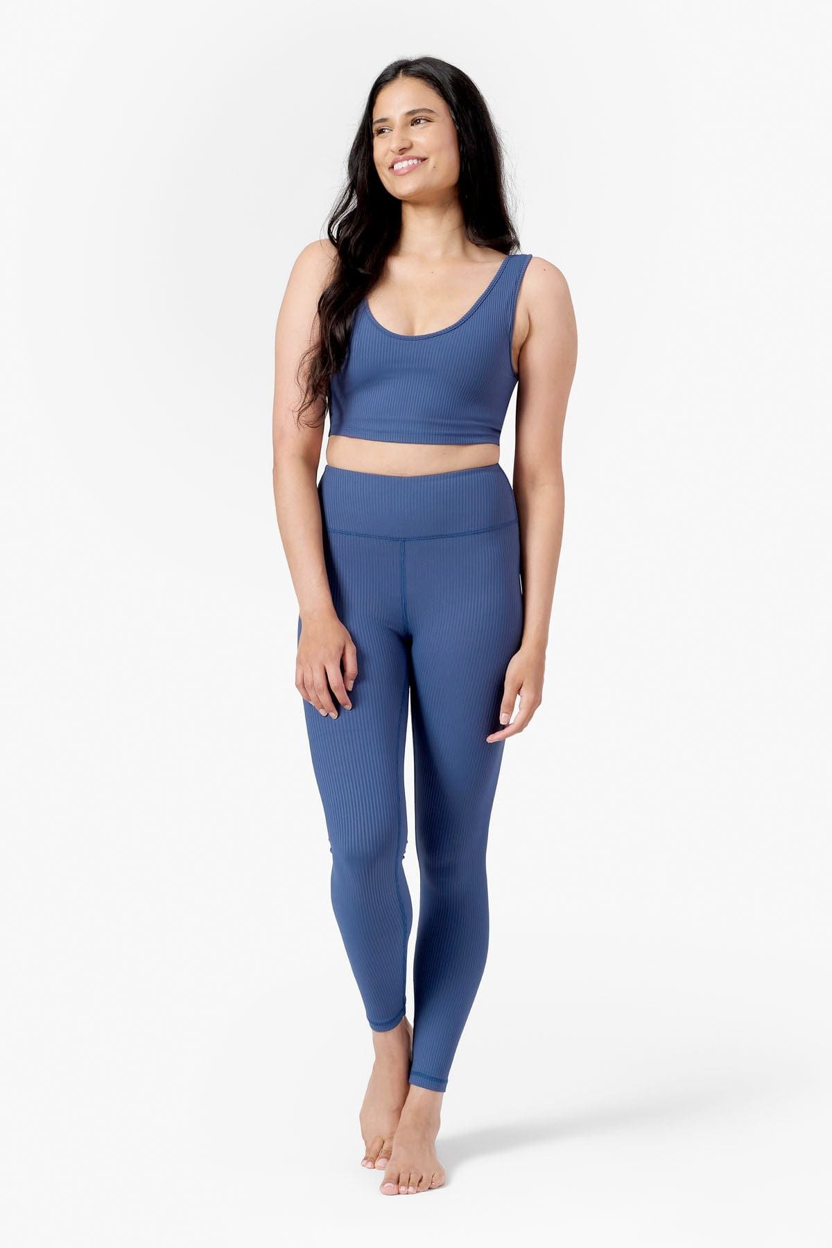 a woman wearing a blue low scoop crop top with lining and a matching blue ribbed pair of leggings