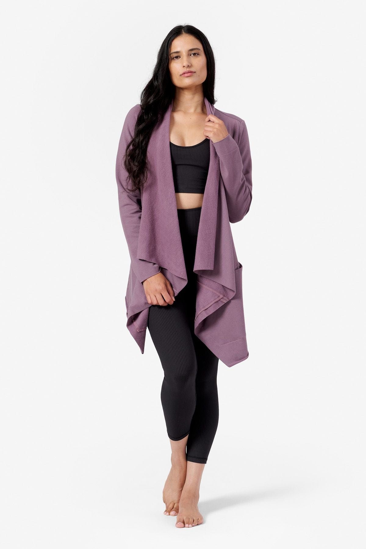 a woman wearing a purple draped jacket made from fleece and a black ribbed crop top and leggings
