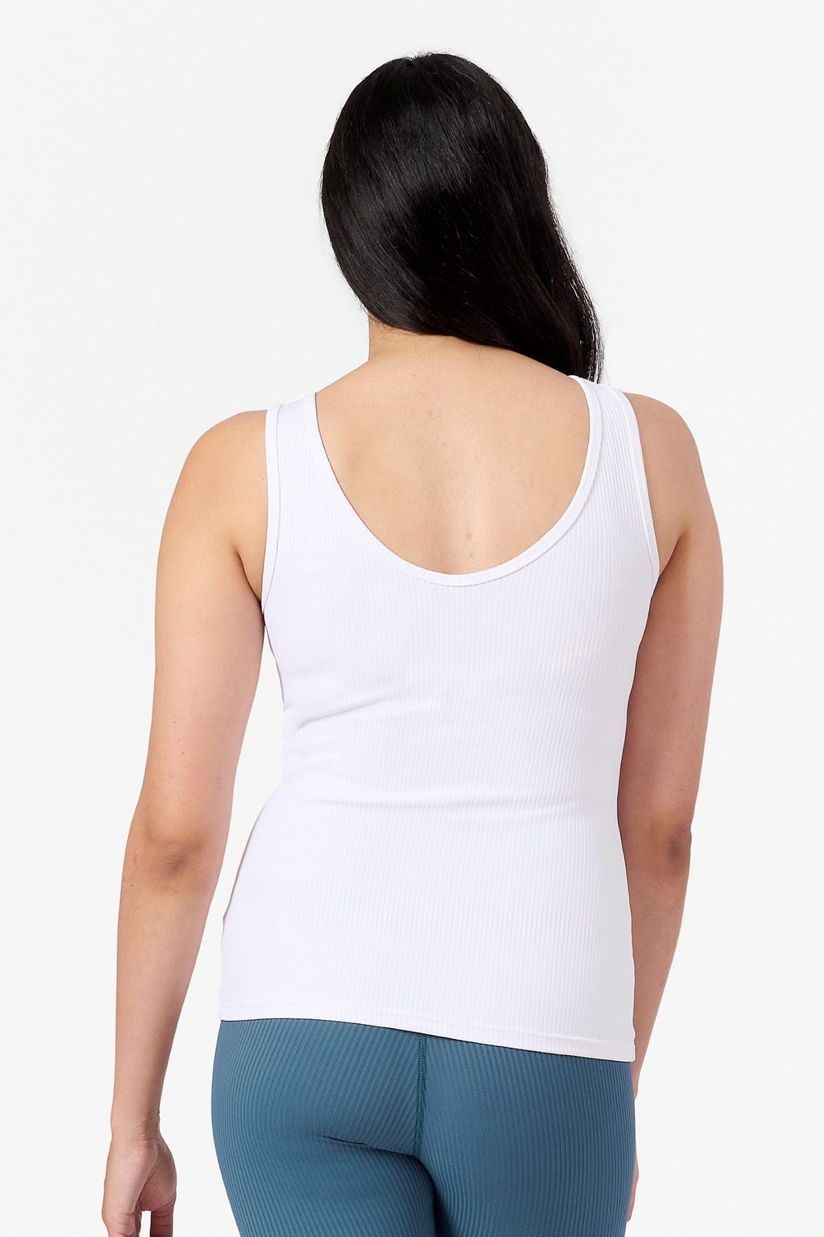 back of a woman wearing a white ribbed sports top and blue leggings 