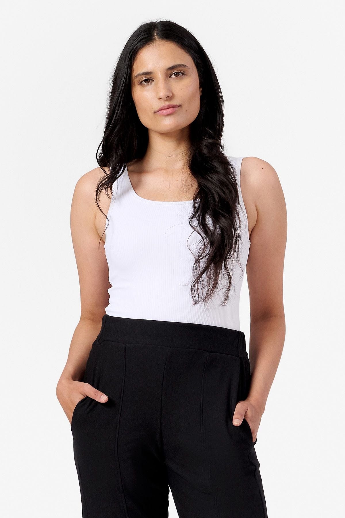 a woman wearing a white ribbed tank top and black work pants