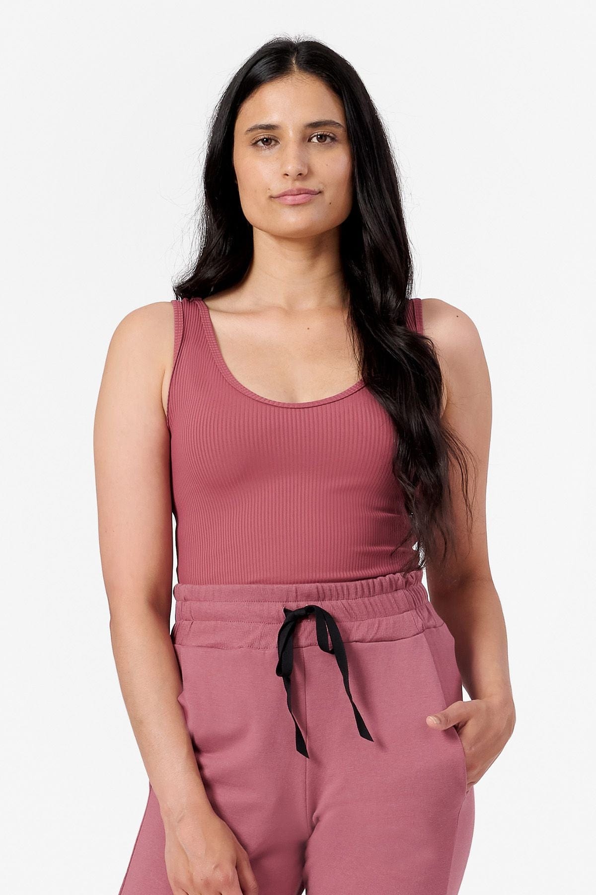 a woman wearing a ribbed pink tank top with a low scoop neck line. 