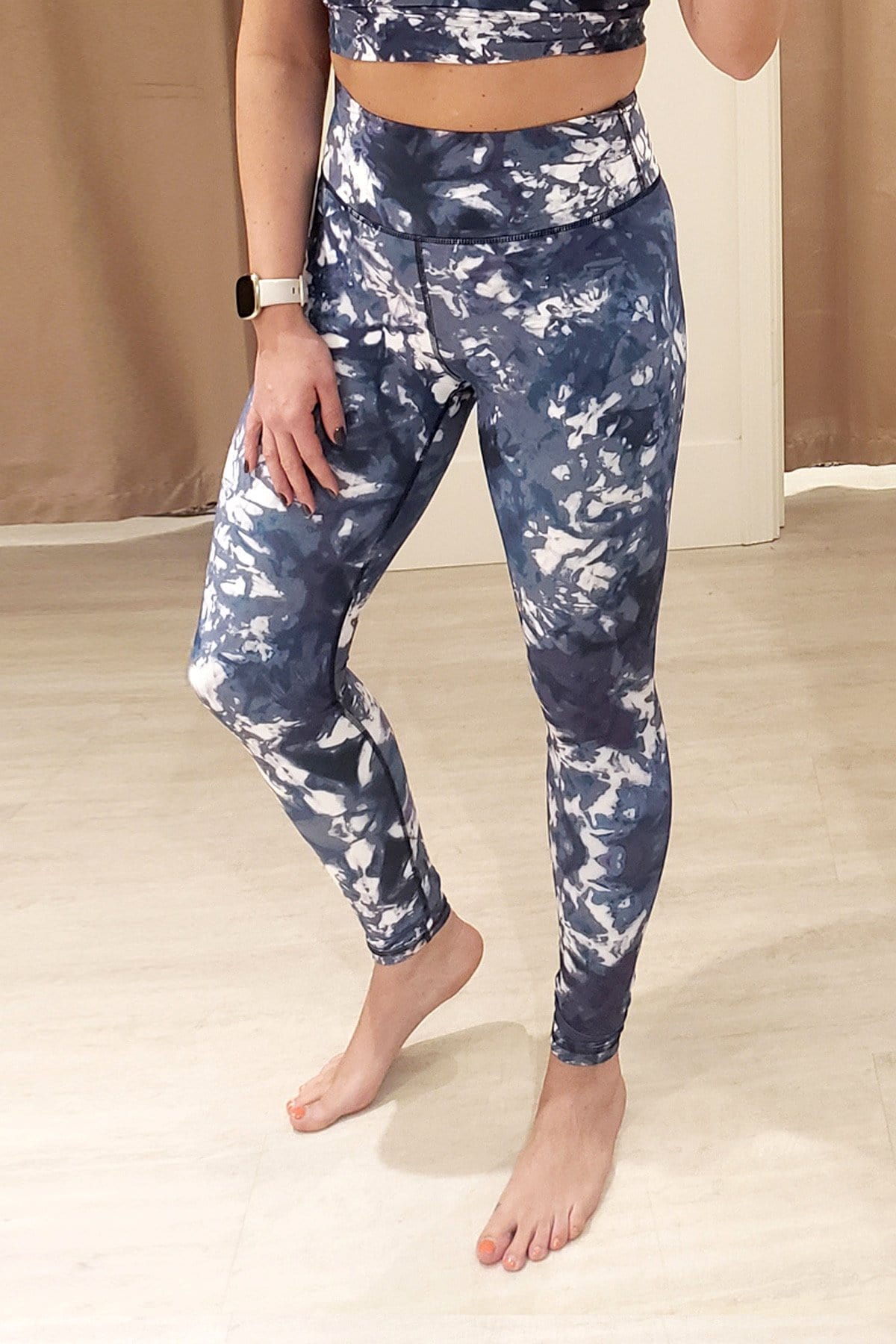 A woman wears a Fitbit, sports bra and pair of DAUB's limited edition Riley Leggings in a blue & white tie-dye print at DAUB's South Granville Flagship.