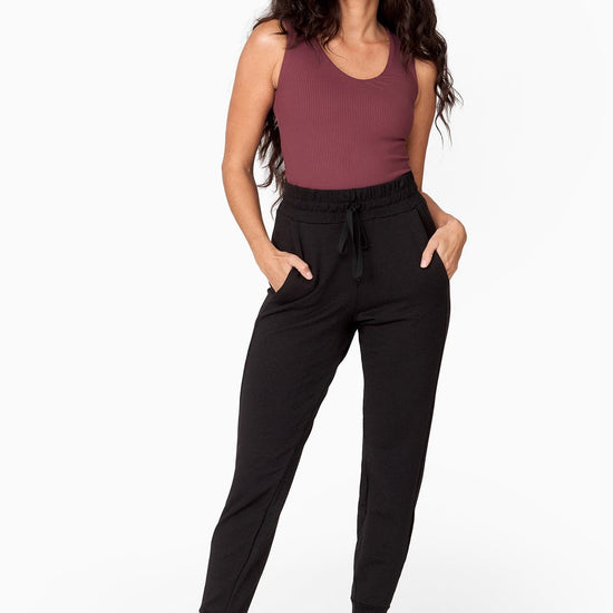 a woman with dark brown long hair wears a brownish purple tank top tucked into a black high waisted jogger