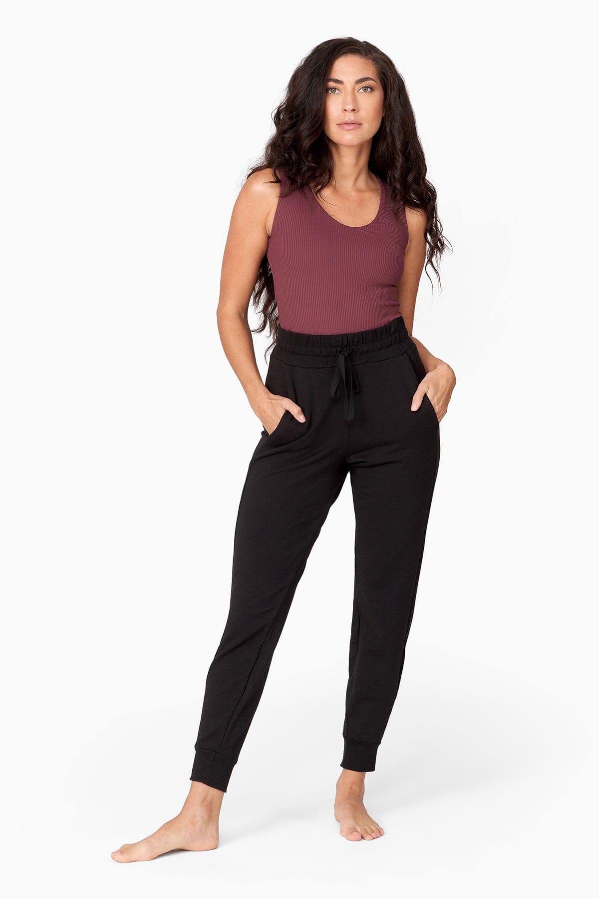 a woman with dark brown long hair wears a brownish purple tank top tucked into a black high waisted jogger