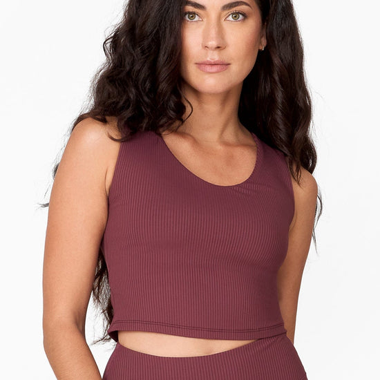 woman with long wavy brown hair wears a muted brownish/purple ribbon tank top