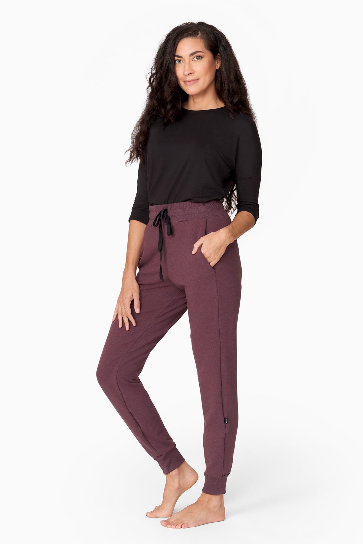 a woman with brunette wavy hair wears a 3/4 sleeve black shirt with a brownish purple jogger pant