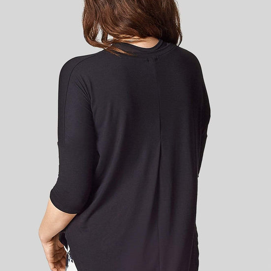 A brunette women is wearing a 3/4 length sleeve tee shirt with a pleat in the back starting at the bust.