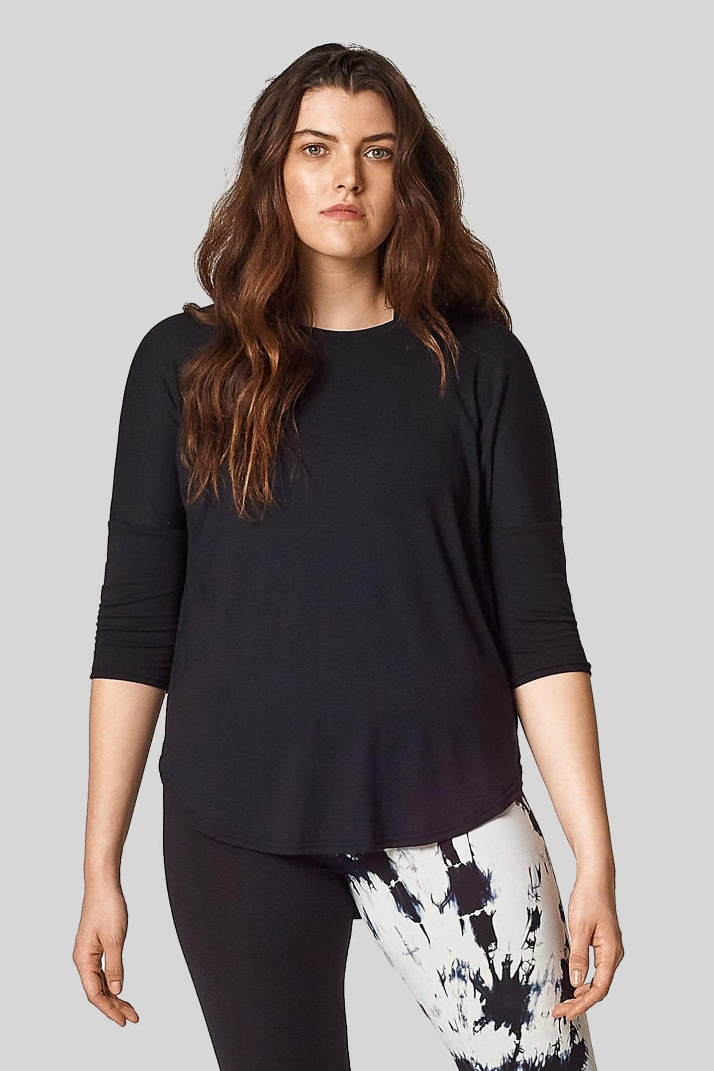 A model wears a t-shirt with 3/4 length sleeves in black with a hi-lo hem (longer in the back).