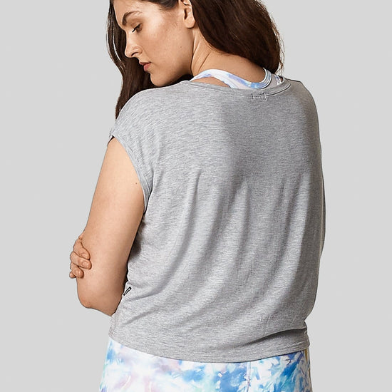 The back view of a brown haired woman wearing a heather grey box tee with printed blue bike shorts.