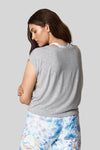 The back view of a brown haired woman wearing a heather grey box tee with printed blue bike shorts.