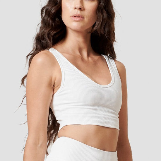 A woman looking over her shoulder modeling a white reversible top. 