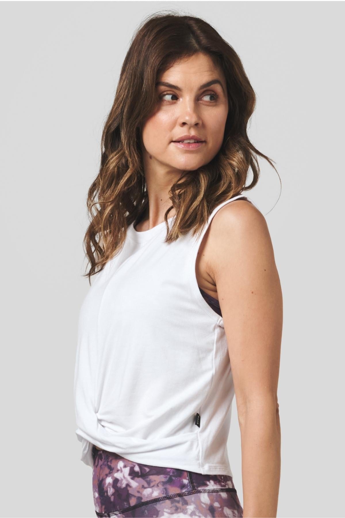 Side of a women wearing a white tank top and tie-dye printed legging.