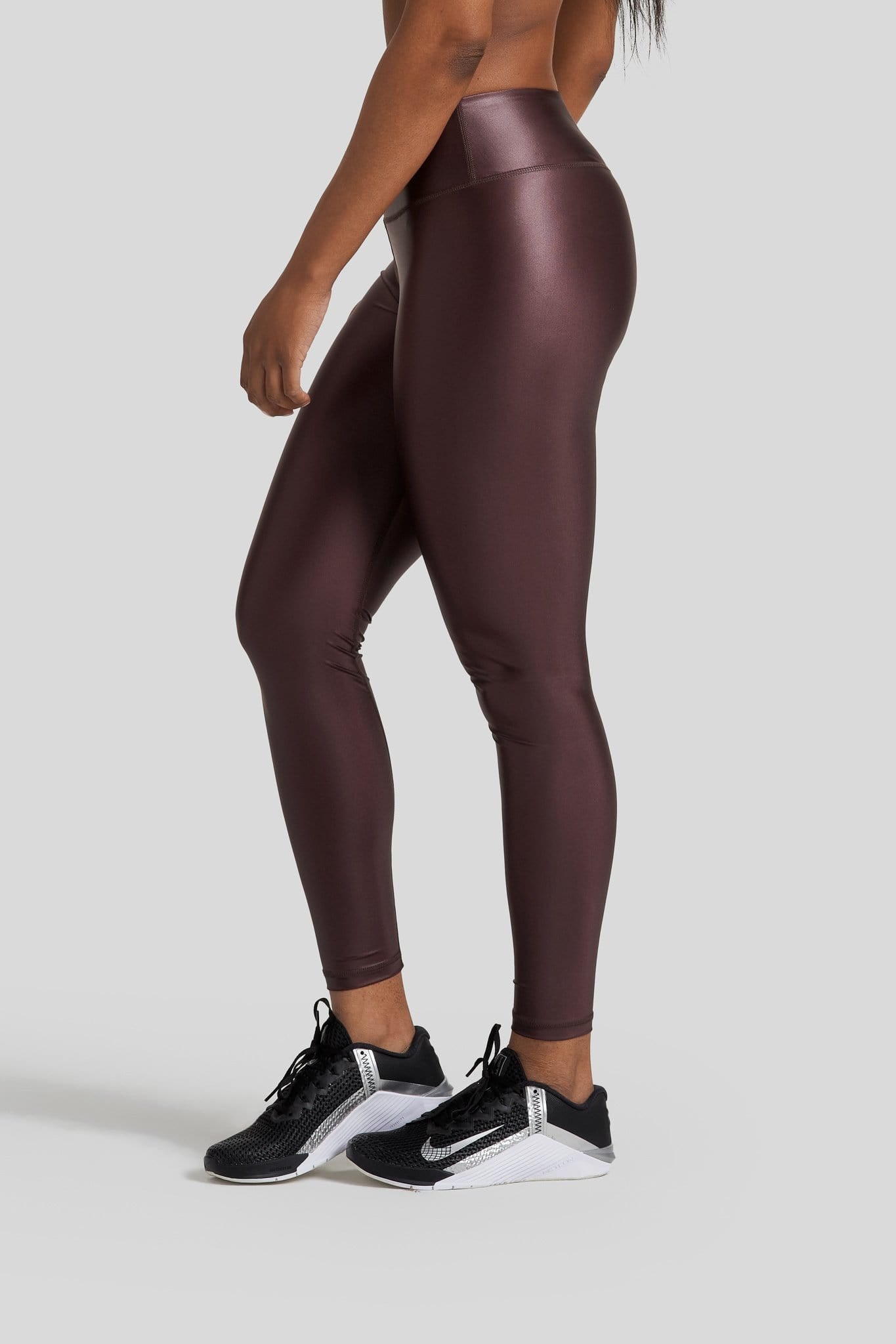 The side profile of a woman's legs are shown wearing hi gloss brown leggings