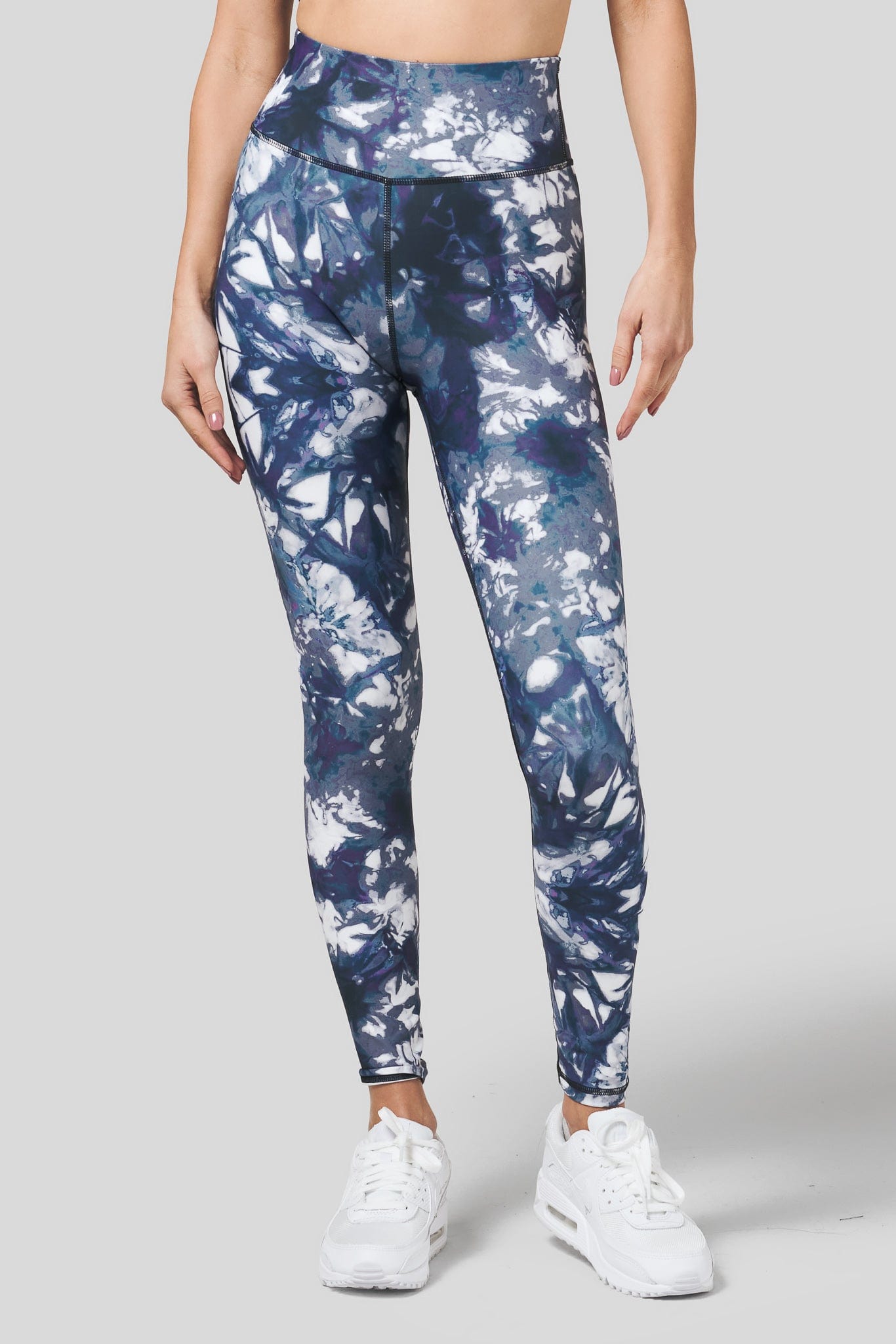 A woman models a pair of crisp white sneakers paired with a pair of blue leggings in a tie-dye print.