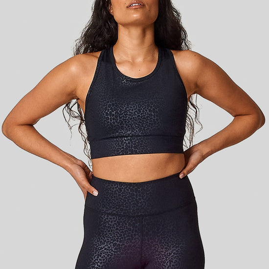 A matching cheetah sports bras & leggings set on a woman with her hands on her hips.