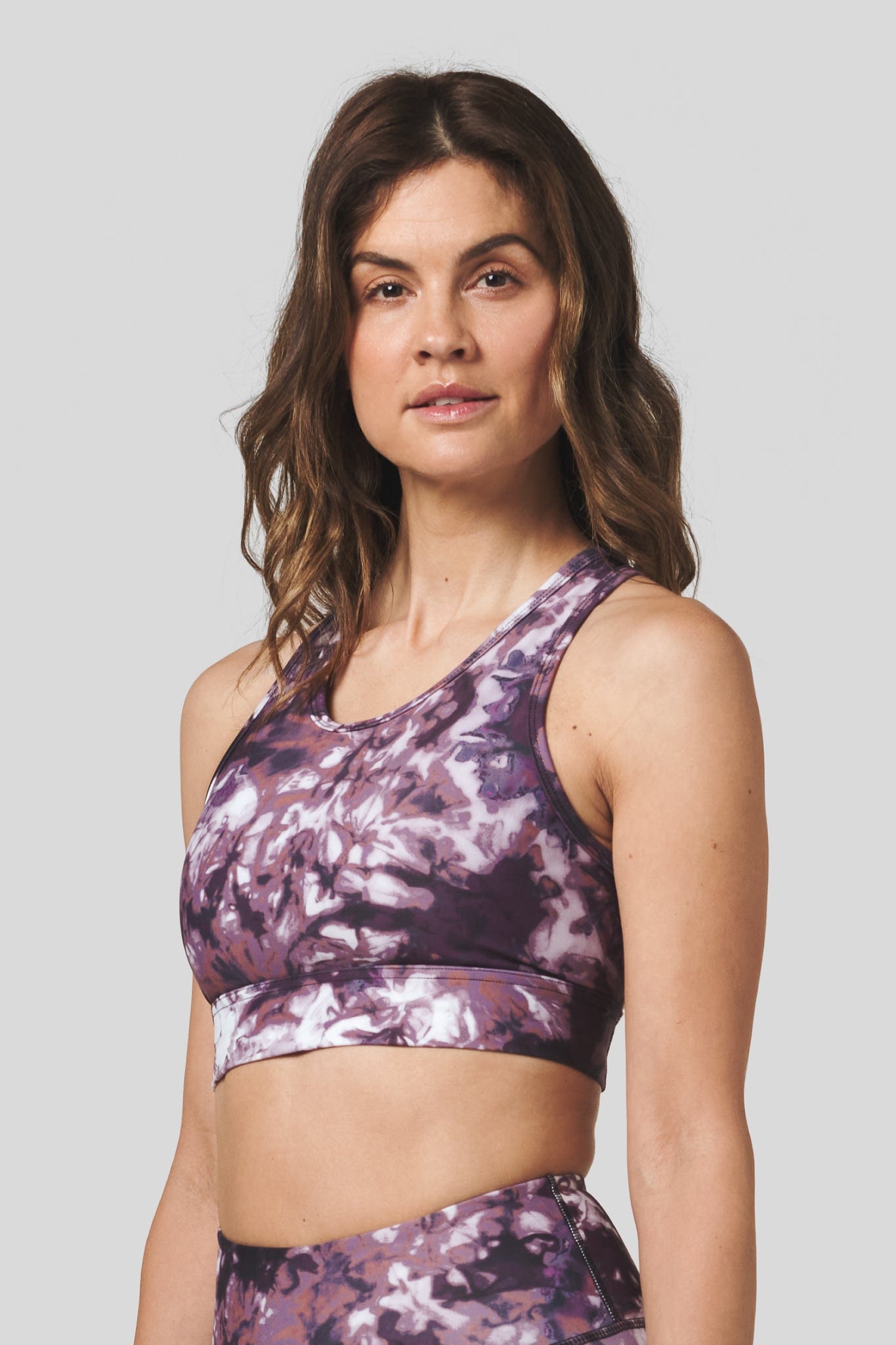 A brunette woman wears a tie dye activewear sports bra and yoga legging set.