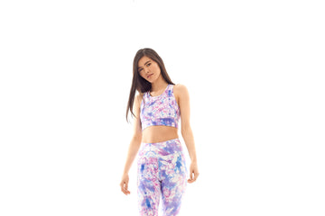 Woman stands in tie-dye purple workout set with purple racerback sports bra and high-waisted purple workout leggings.