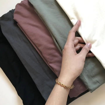 a woman's hand touching a row of folded tees in white, green, brown, grey and black