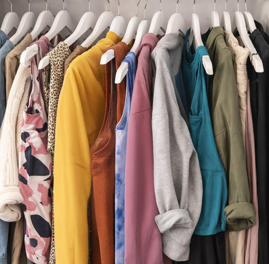 A messy closet with many colours and prints on white hangers. It shows this kind of wardrobe can be hard to navigate.