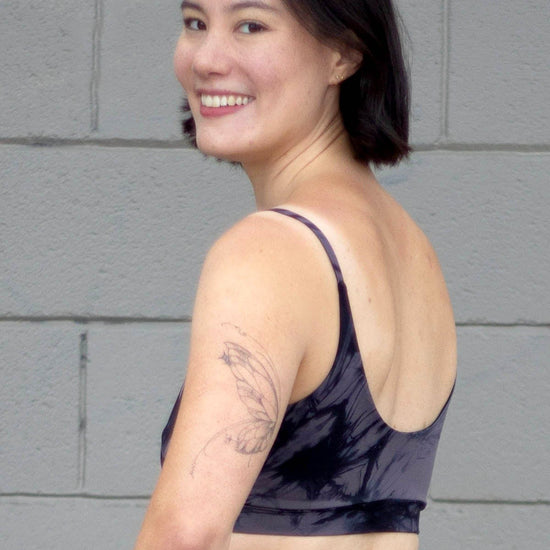 The back of a woman smiling and wearing a grey tie-dye swim top