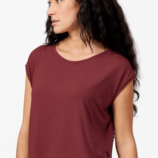 A brunette woman wears a boxy tee made from modal spandex. It is a red top that hangs slightly off the shoulder.