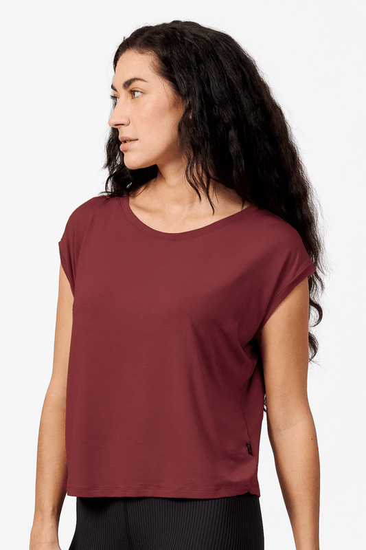 A brunette woman wears a boxy tee made from modal spandex. It is a red top that hangs slightly off the shoulder.