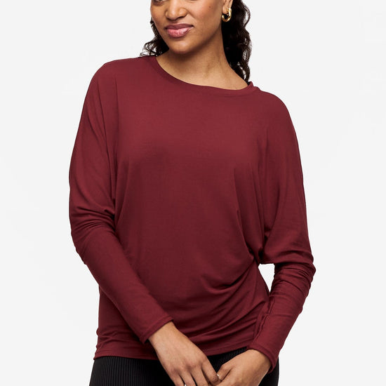 woman wearing a dark red loose sleeve long sleeve shirt with their hands crossed