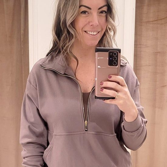 A blonde woman wears a light brown half zipped sweatshirt with ribbed leggings and a sports bra. Each piece is made in Canada.