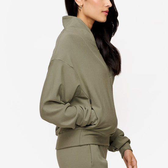 side of a woman wearing a 1/4 zip sweatshirt in green