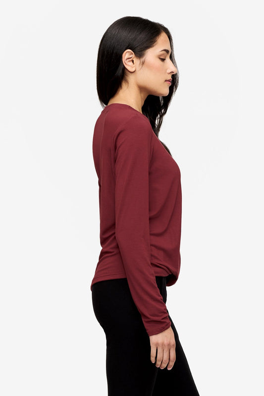 side of a woman wearing a long sleeve shirt with a twist at the front in  deep red