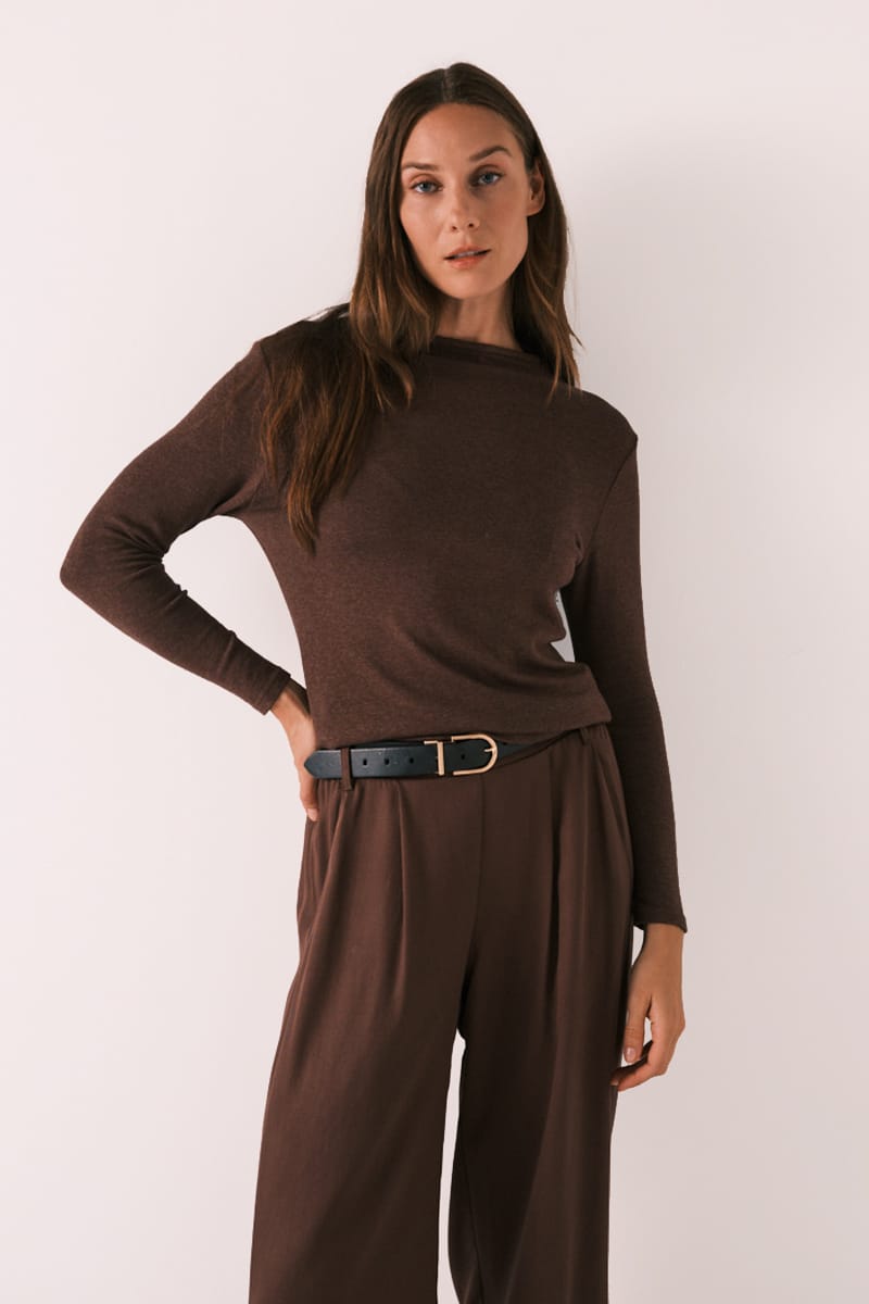 A woman modeling a dark brown long-sleeve mock neck top paired with matching brown wide-leg trousers and a black belt with a gold buckle, set against a plain light background.