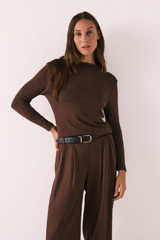 A woman modeling a dark brown long-sleeve mock neck top paired with matching brown wide-leg trousers and a black belt with a gold buckle, set against a plain light background.