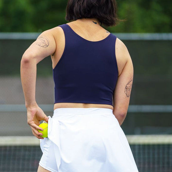 Back of a woman playing tennis wearing a white tennis skirt