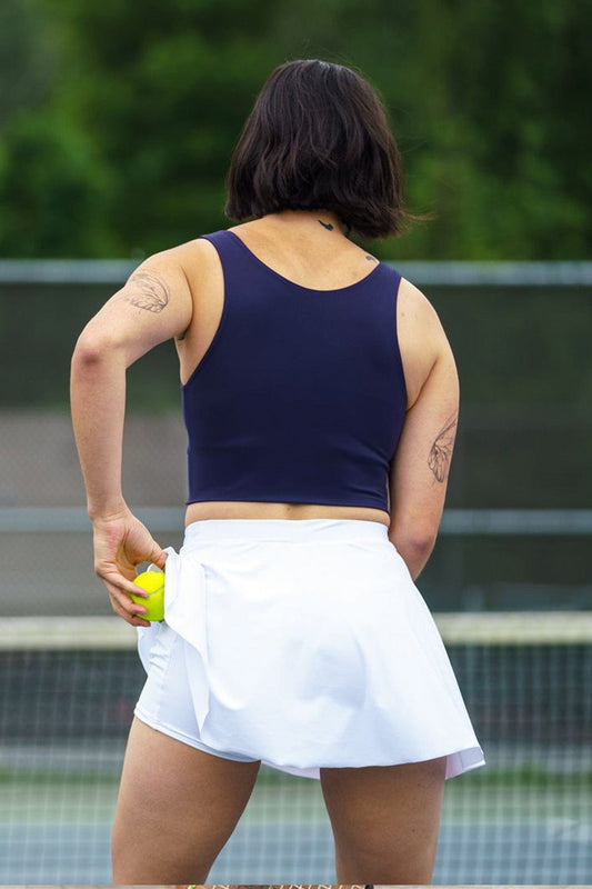 Back of a woman playing tennis wearing a white tennis skirt