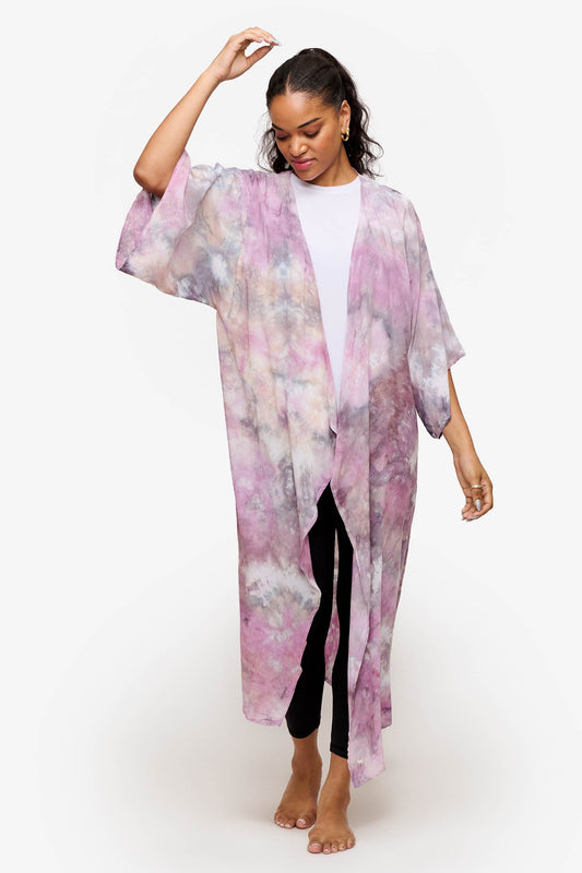 A young woman wears a multi-coloured tie-dyed robe with a white tee-shirt and athletic leggings.