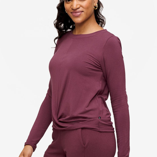 side of a woman wearing a deep pink long sleeve top with twist in the front 