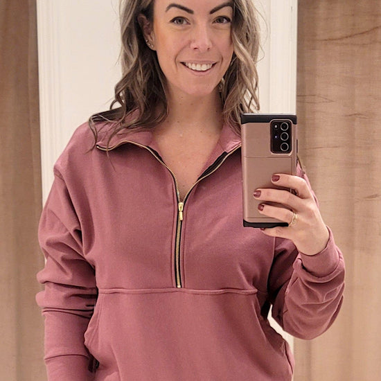 The designer, Lexi Soukoreff, wears a new pink sweatshirt from DAUB with a gold zipper and front pocket.