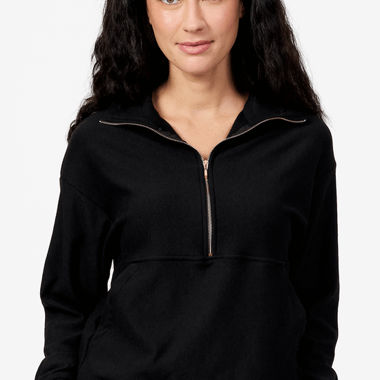 Woman wearing a black half zip sweatshirt with her hands on the pockets