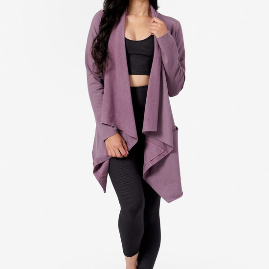 a woman wearing a purple draped jacket made from fleece and a black ribbed crop top and leggings