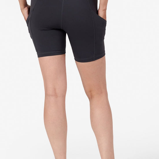 a woman's legs is wearing grey bike shorts and her hands are in the side pockets of the shorts