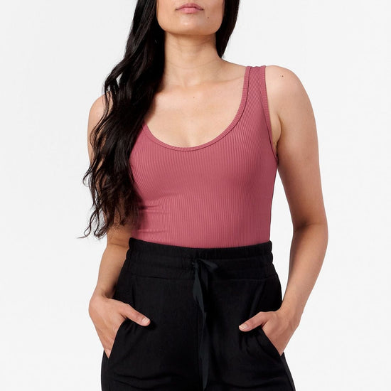 woman wearing a pink ribbed tank top with a low scoop neck and black joggers