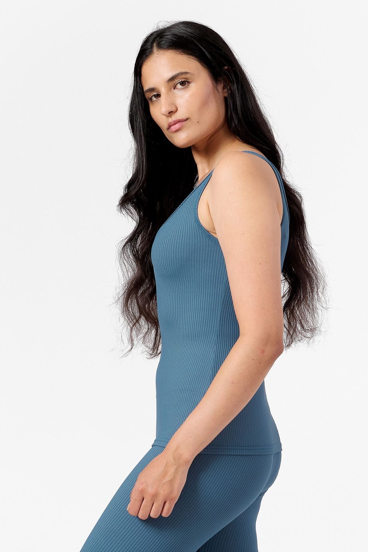 side view of a woman wearing a hip length ribbed teal tank top with matching ribbed  leggings