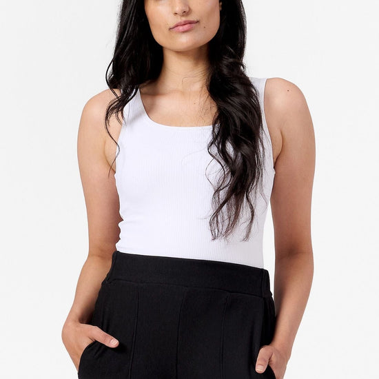 a woman wearing a white ribbed tank top and black work pants